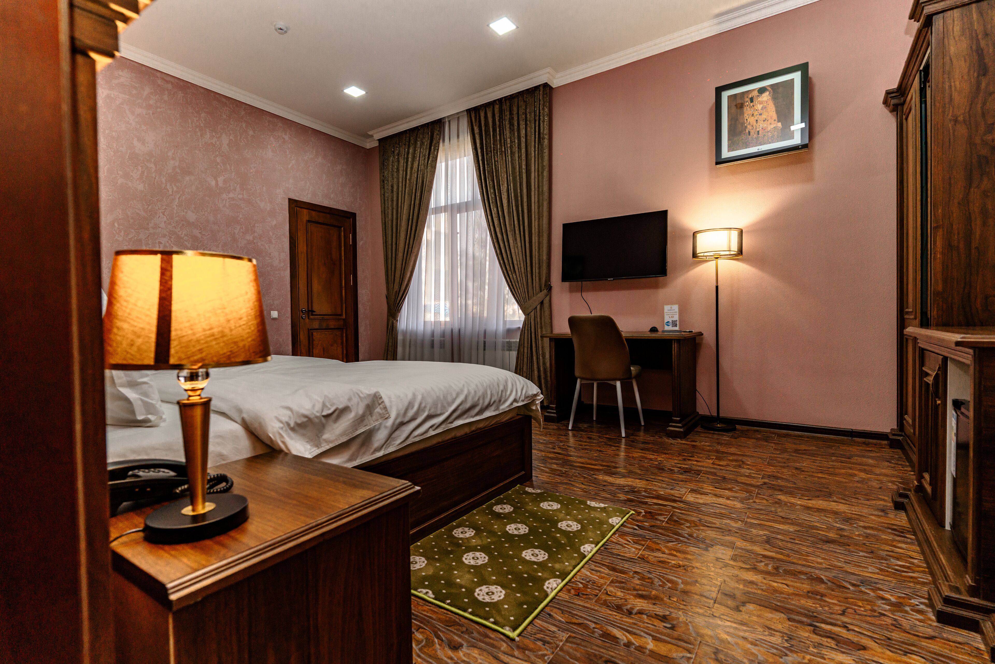 Quarto de hotel com cama, escrivaninha, cadeira, televisão e abajur.