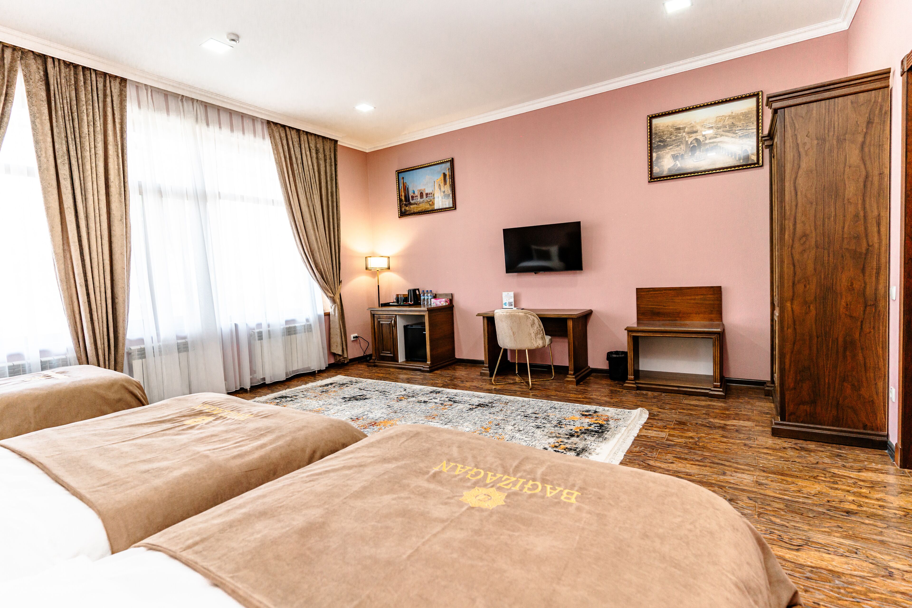 A hotel room with two beds, a desk, a chair, a television, and a large window with curtains.