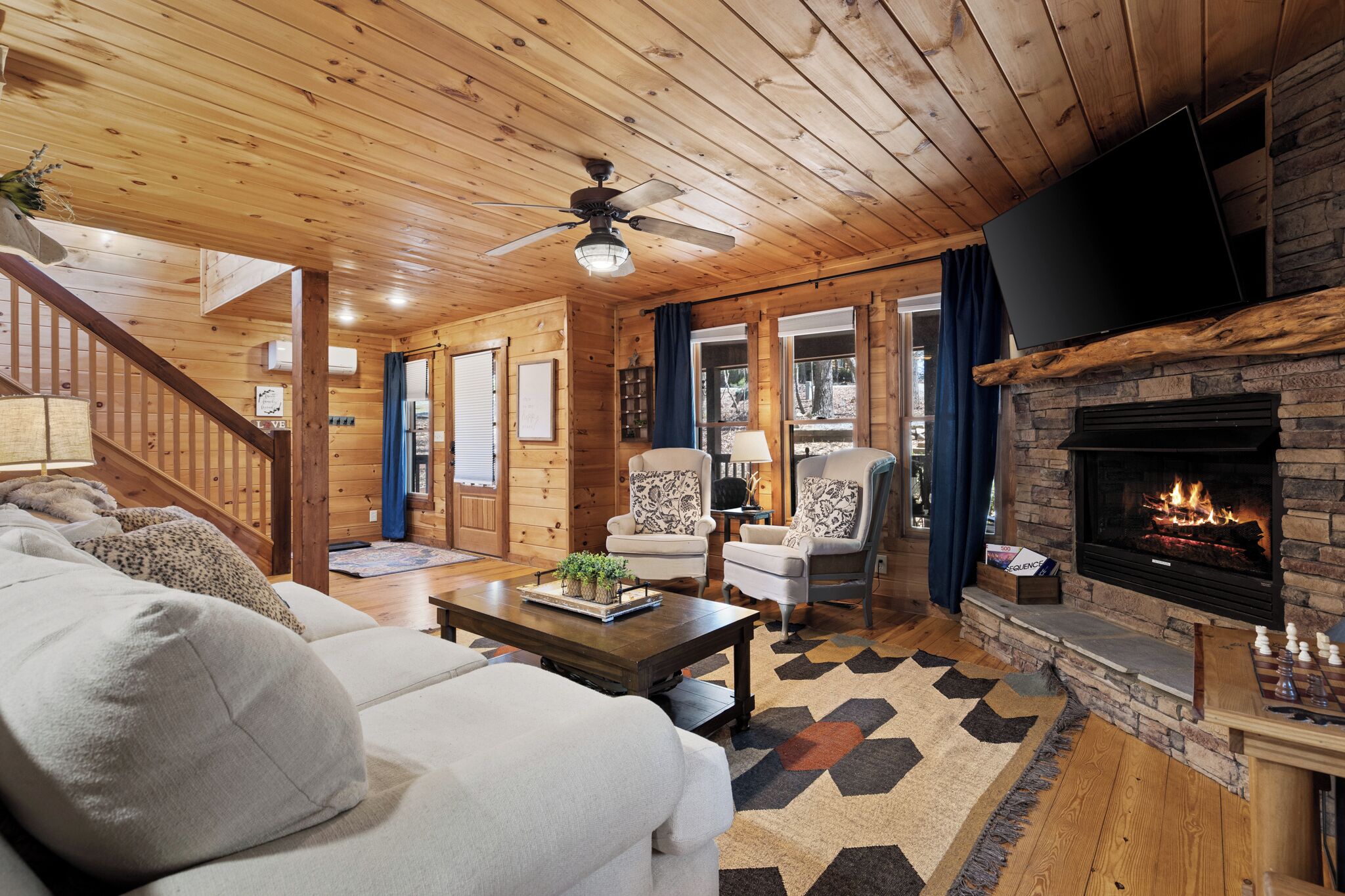 L’intérieur d’un chalet accueillant, avec une cheminée, un plafond en bois et un canapé agrémenté de coussins.