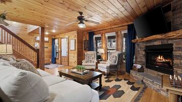 L’intérieur d’un chalet accueillant, avec une cheminée, un plafond en bois et un canapé agrémenté de coussins.