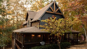 Une cabane rustique dotée d’un toit à forte pente, d’une terrasse en bois et d’un petit porche.