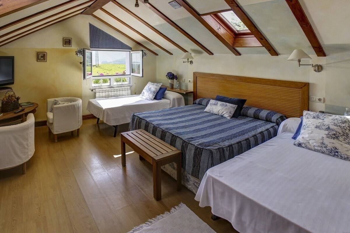 Een slaapkamer met twee bedden, een houten bankje, een televisie en een raam met uitzicht op het landschap.