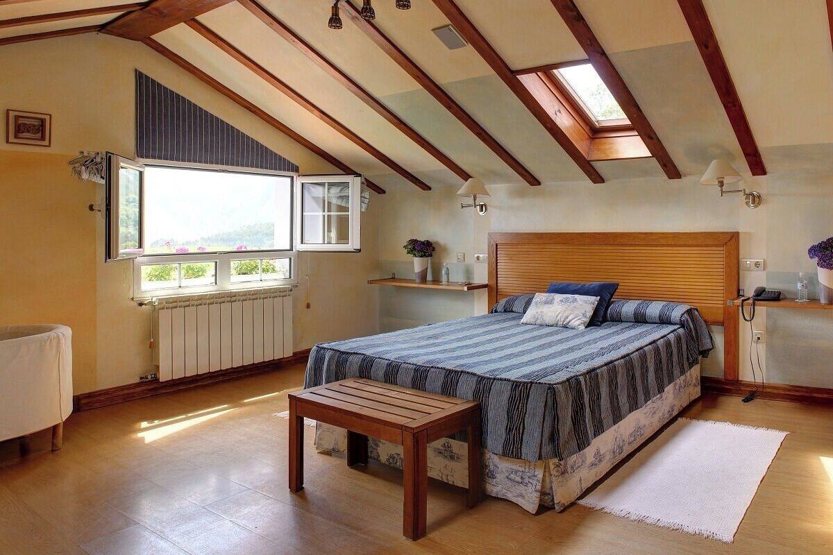 Een slaapkamer met een houten bed, een raam met uitzicht, een nachtkastje en een radiator.