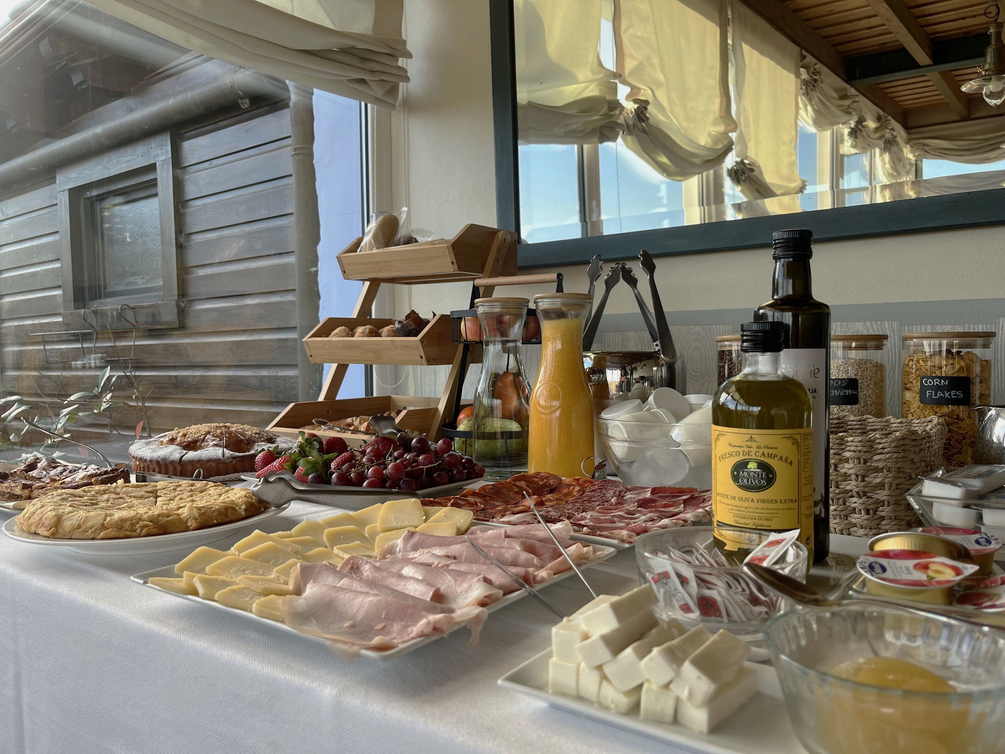 Un bufé con diversos quesos, carnes, frutas y una botella de aceite de oliva.