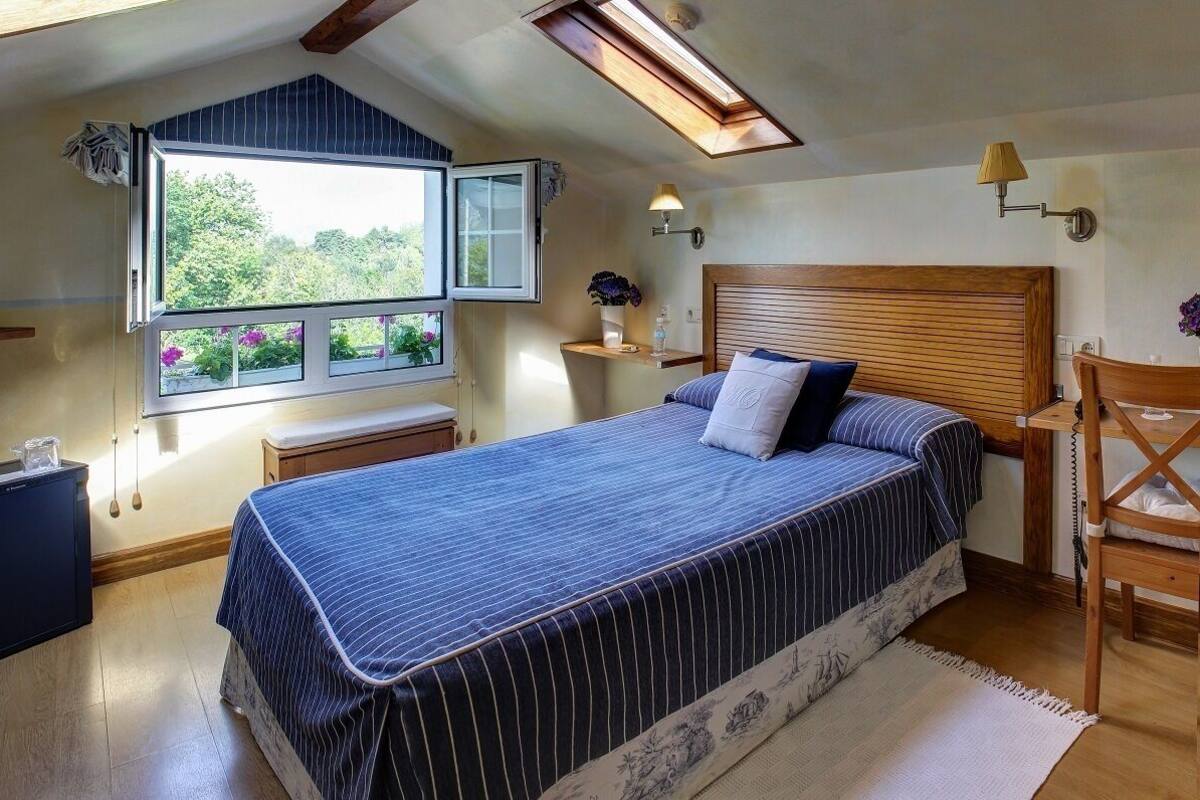 Een slaapkamer met een groot bed, dakraam, nachtkastje en een raam met uitzicht op groen.