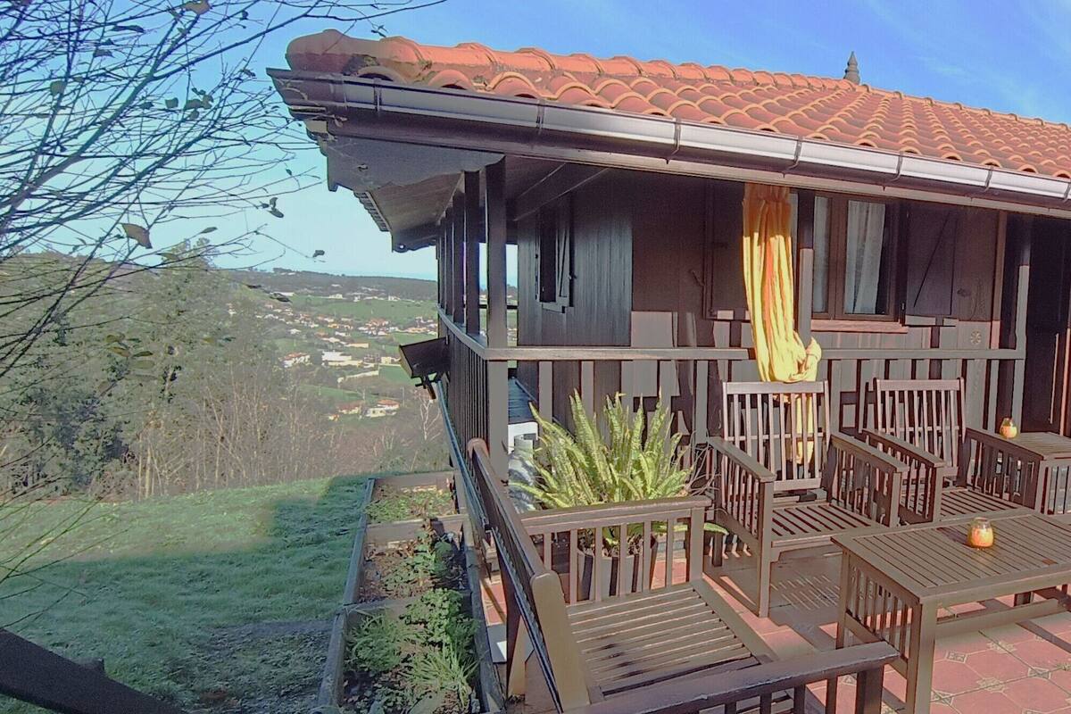 Een houten balkon met een betegeld dak, houten meubilair en uitzicht op een glooiend landschap.