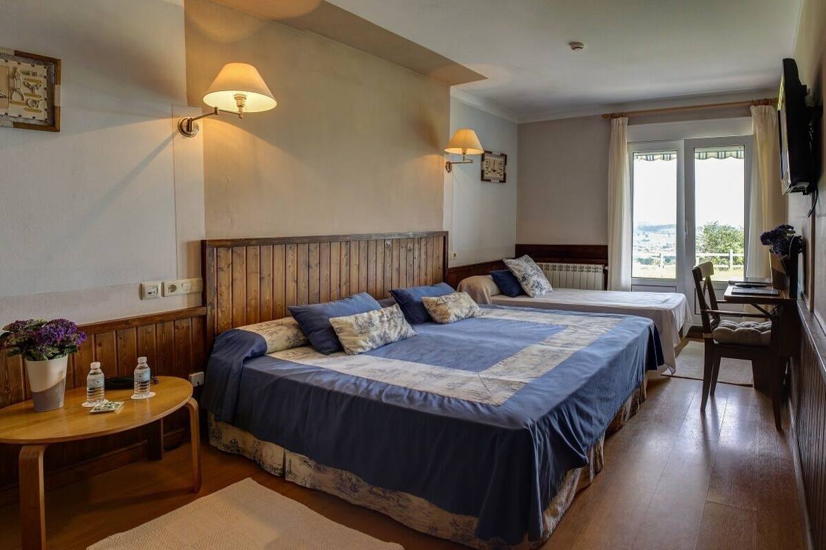 Hotelkamer met twee bedden, een houten hoofdbord, een tafeltje met een plant en uitzicht op het landschap door een raam.