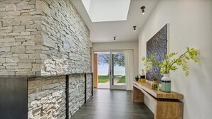 A modern interior with a stone wall, a wooden bench, and a view through glass doors to the outdoors. - Clay Banks Lakehouse · Door County Lake House 50 min from Lambeau Field (Algoma)