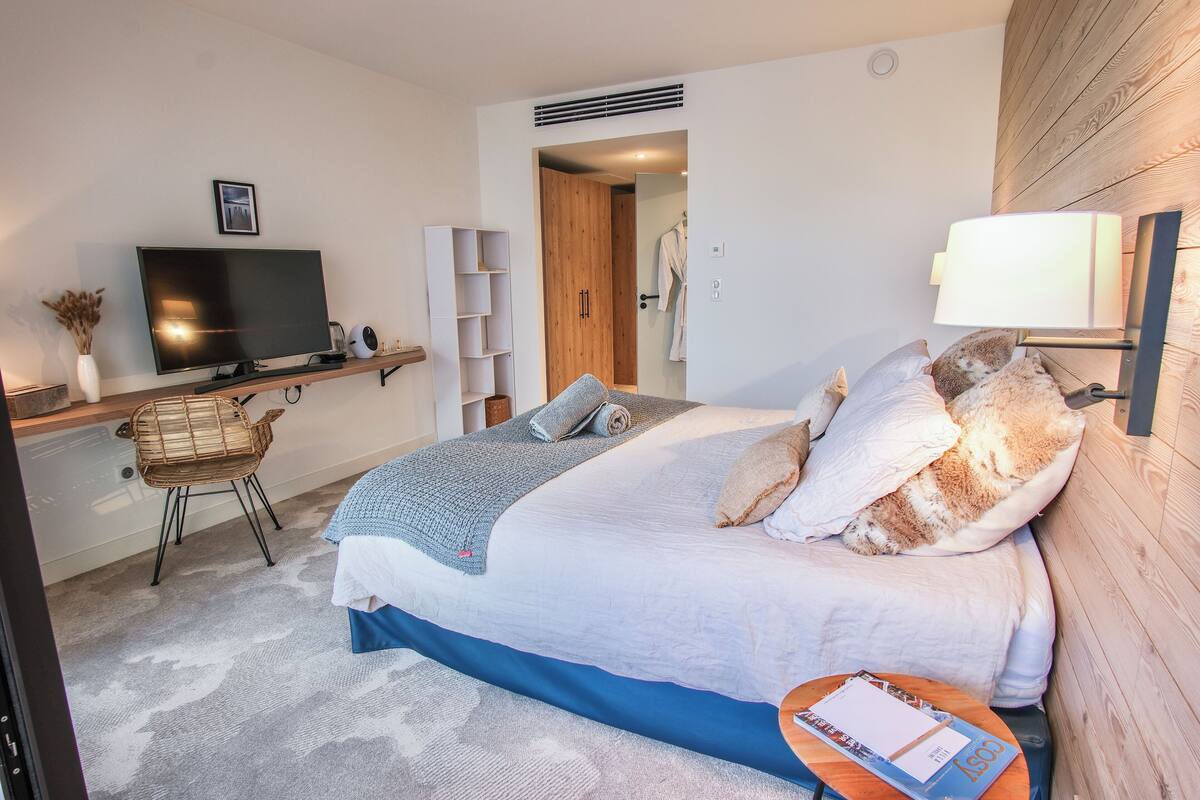 A modern hotel room with a large bed, a television, a desk with a chair, and a wooden wall.