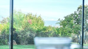 Uma chávena de chá sobre uma mesa, com vista para uma zona relvada e árvores através de uma janela.