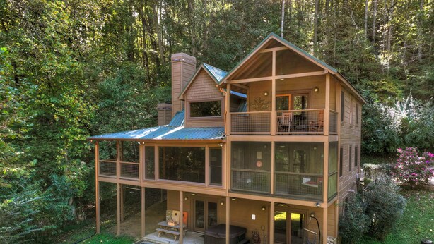 Une cabane en bois à deux étages, dotée d’un balcon et entourée d’une forêt dense.