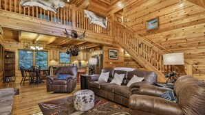 L’intérieur d’une cabane en rondins comprend un coin repas, un salon avec des meubles en cuir, un escalier et une cuisine.