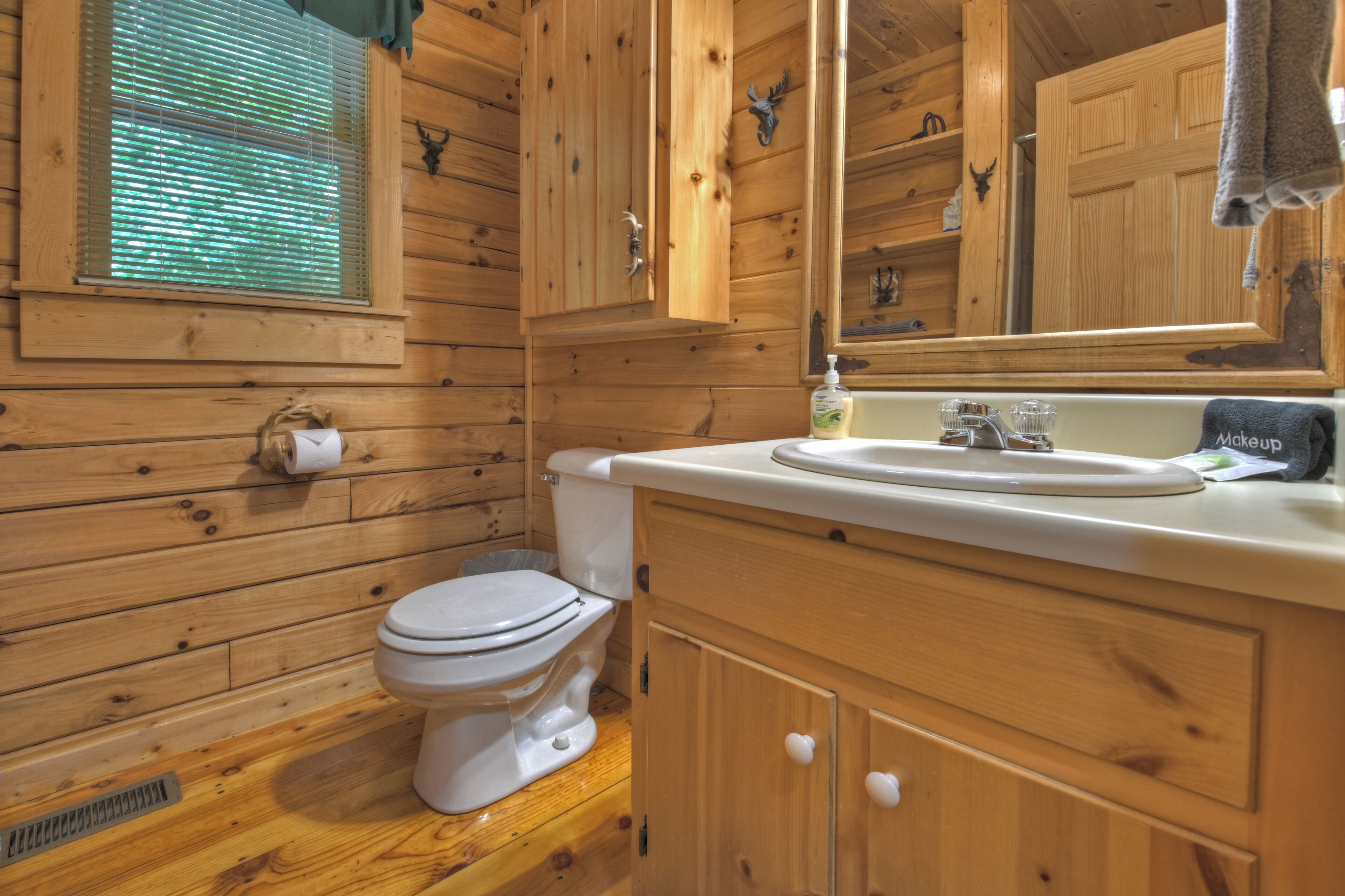 Une salle de bain rustique, aménagée dans une cabane en bois, avec des toilettes, un lavabo et un miroir.
