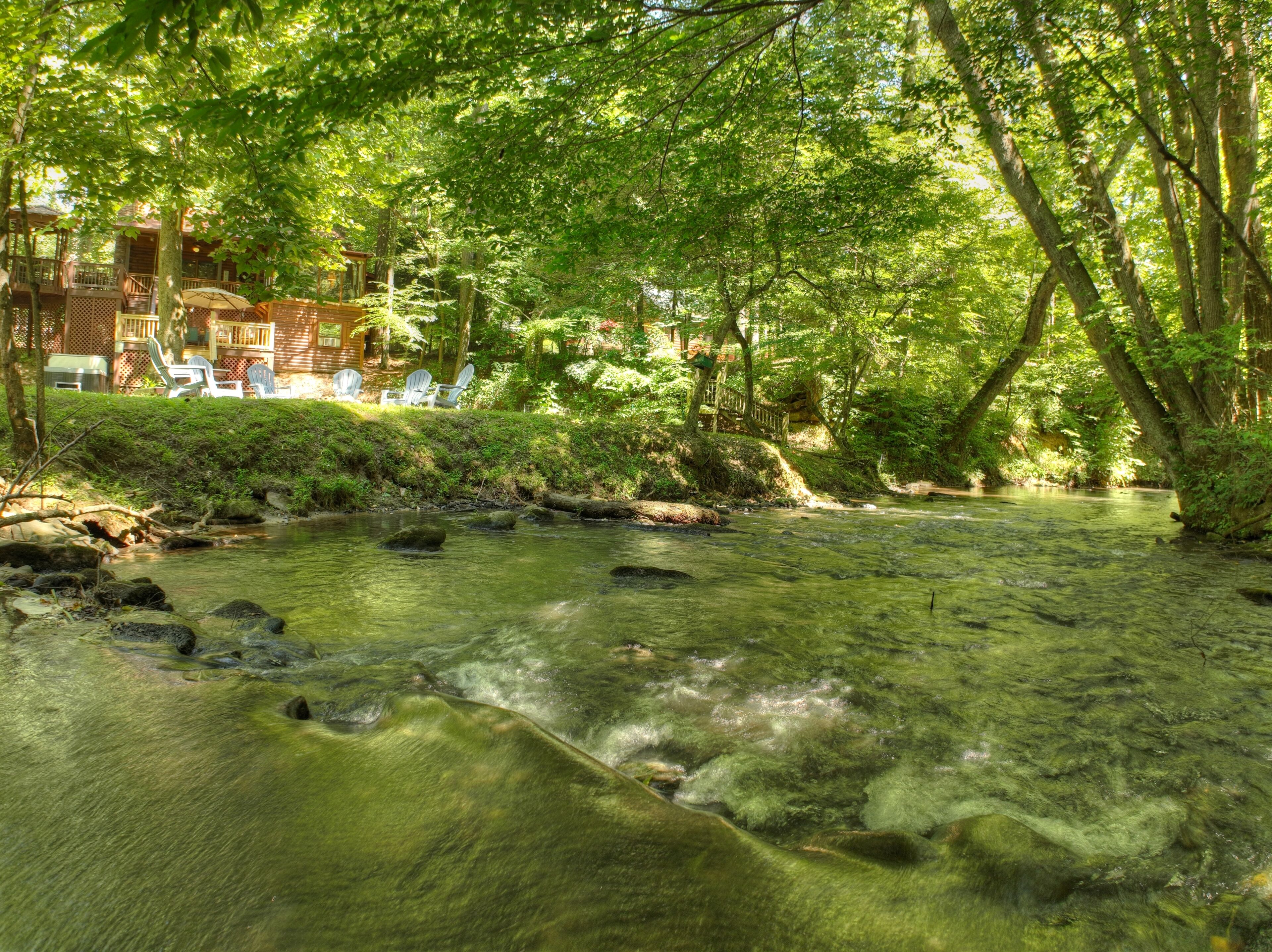 Un cadre paisible au bord de la rivière, avec une terrasse en bois et des chaises donnant sur l’eau.