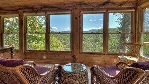 A wooden cabin with wicker furniture, large windows, and a view of the forest. - Amazing Mountain Views! Fenced Yard, Hot Tub, Game Room with Arcade Game & Pool Table, Firepit, Fishing Pond - View Point (Blue Ridge)