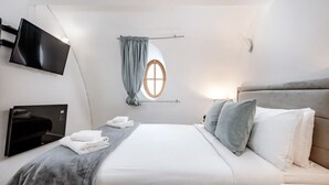 Moderni hotellihuone, jossa on sänky, seinälle asennettu televisio, ikkuna verhoilla ja yöpöytä.