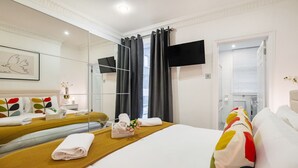 A hotel room with a large bed, a flat-screen TV, a mirror, and a view of the bathroom. - Charming Flat in Covent Garden (Greater London)