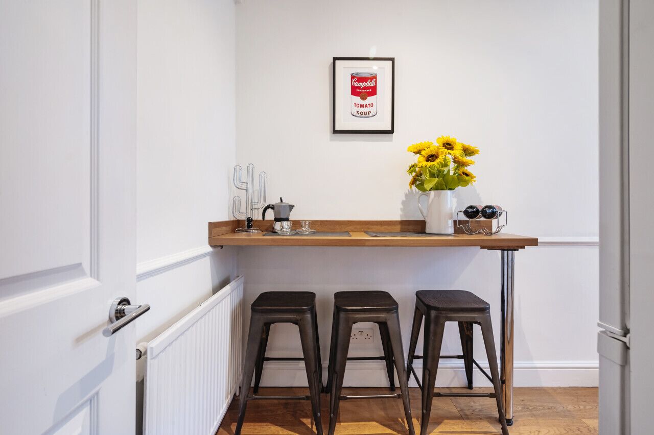 Een keuken met een wit aanrecht, een bord met een Campbell's Tomatensoep reclame, een vaas met gele bloemen, en drie krukken.