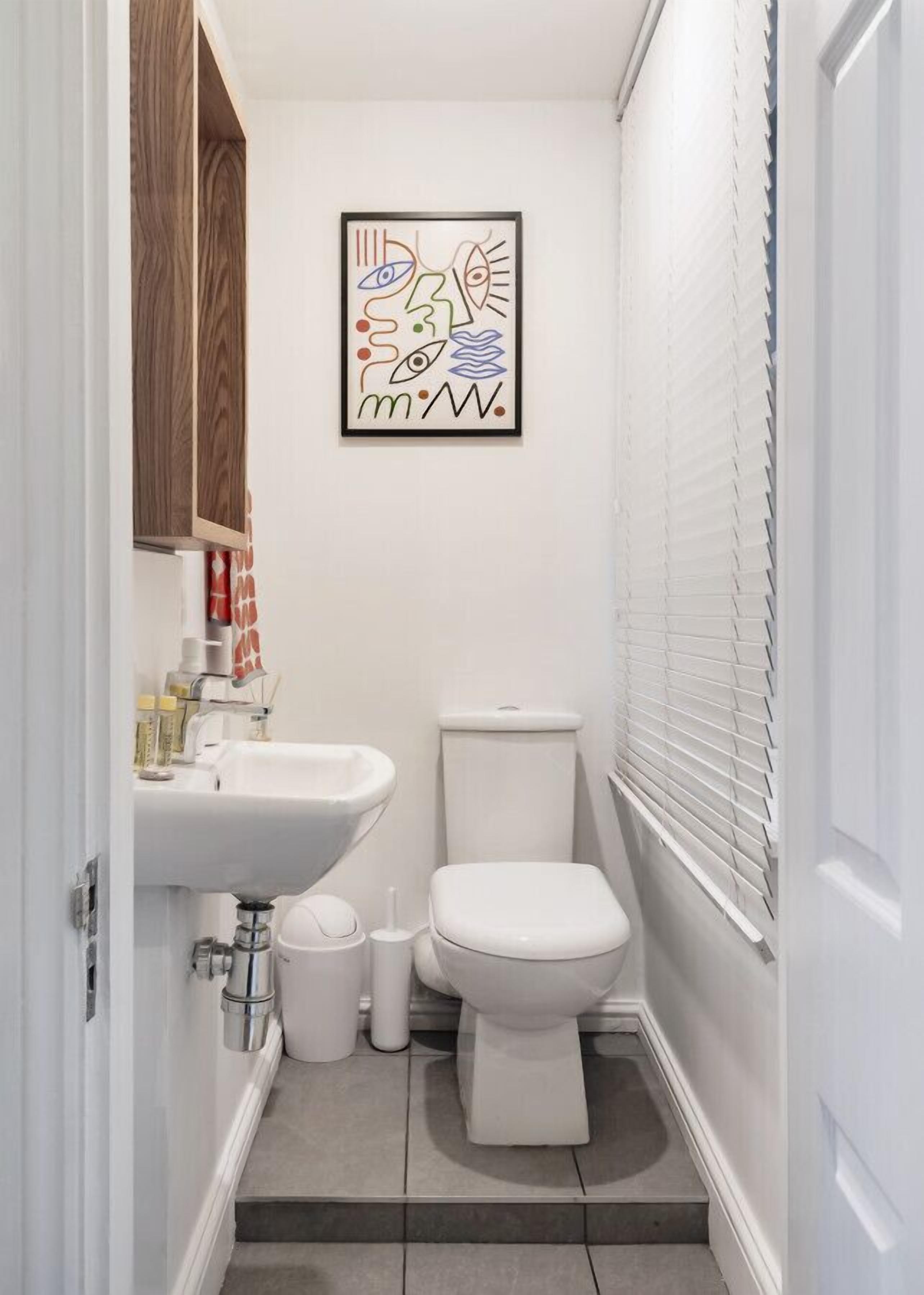 Un bagno piccolo e moderno con lavandino, vaso e un'opera d'arte astratta incorniciata al muro.