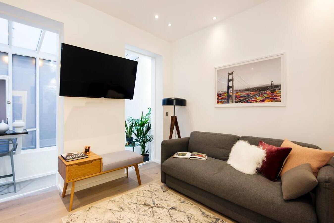 Ein modernes Wohnzimmer mit einem grauen Sofa, einem flachbildschirmfernseher an der Wand, einer Bank und einer Stehlampe.