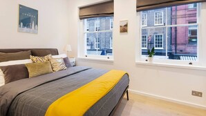 Ein modernes Schlafzimmer mit einem großen Bett, zwei Fenstern mit Blick auf Gebäude und einem Stadtplakat an der Wand.