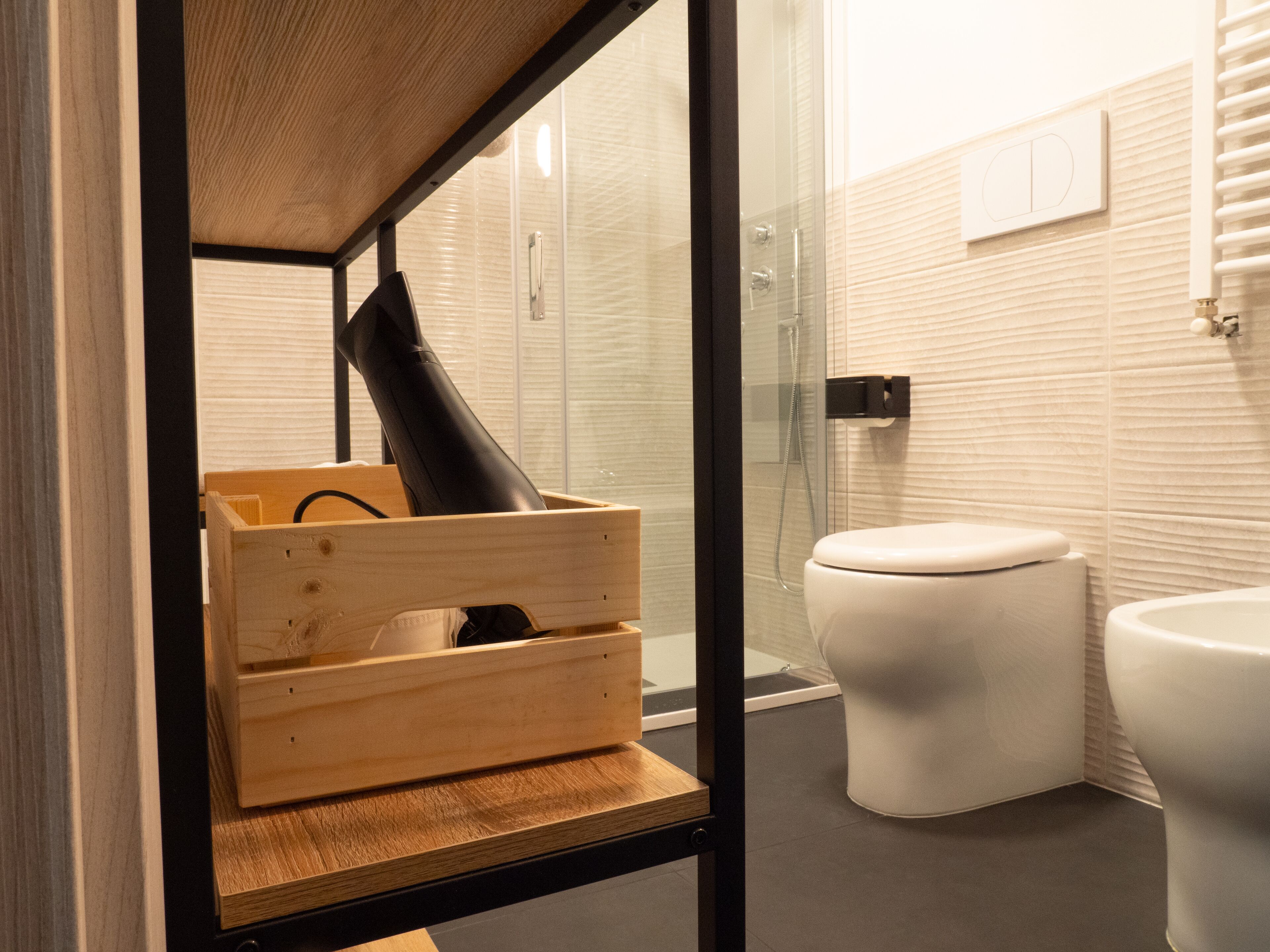 A modern bathroom with a glass shower enclosure, a white toilet, and a wooden storage unit with a black object inside.