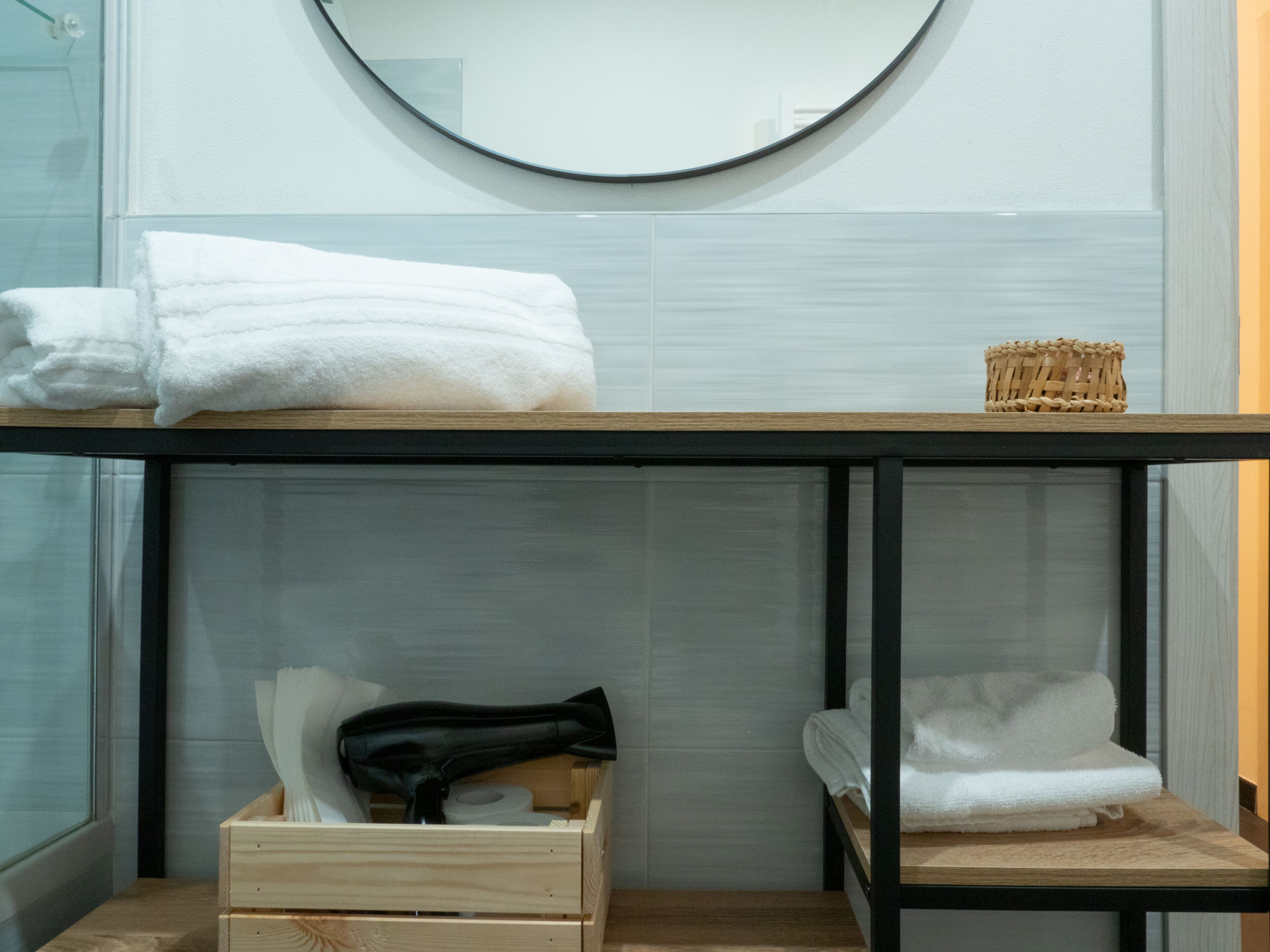A bathroom with a wooden vanity, a round mirror, and a towel rack.