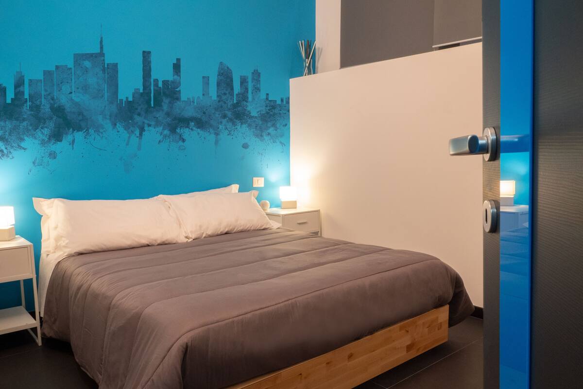 Un dormitorio moderno con un mural de paisaje urbano en la pared, un cabecero de madera y lámparas de noche.