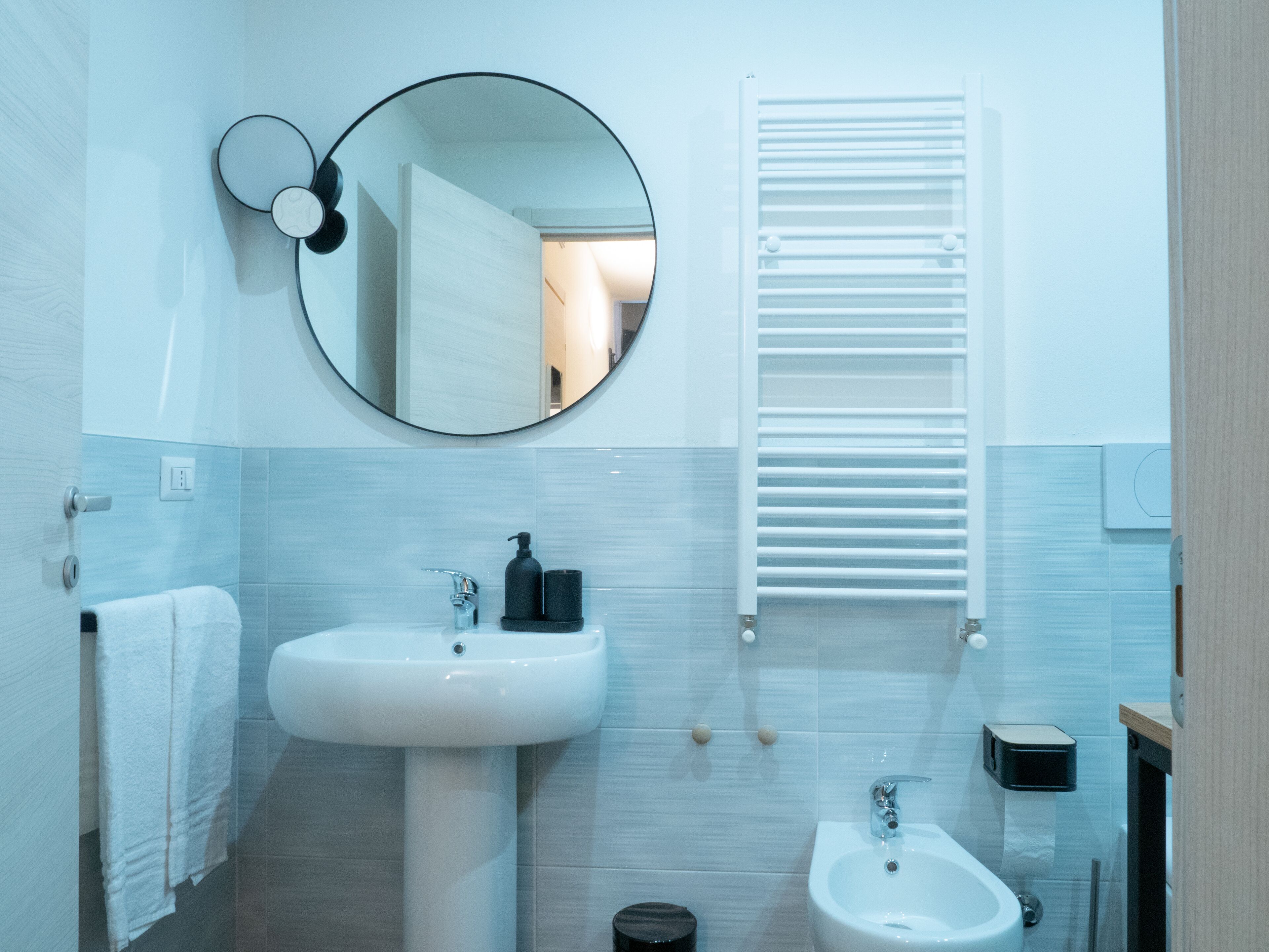Un bagno moderno con un lavandino bianco, un bidet, uno specchio e un porta asciugamani.