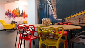 Een moderne vergaderruimte met een ronde houten tafel, kleurrijke stoelen, een stadsgezicht muurschildering en een model treinset.
