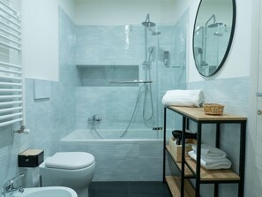 A modern bathroom with a glass-enclosed shower, a white toilet, a sink, and a wooden shelf with towels. - Blocco Sauli (Milan)