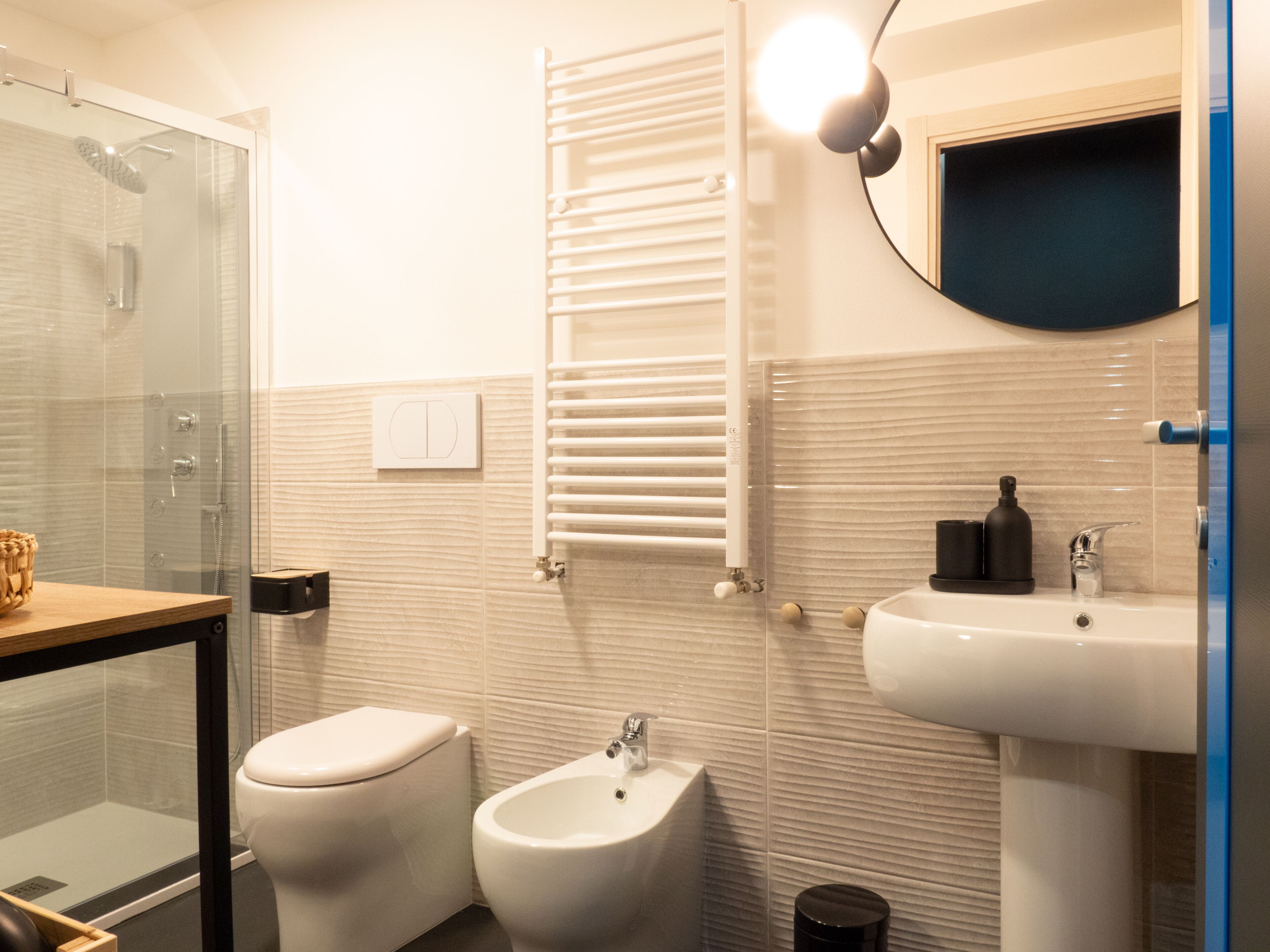 Un baño moderno con cabina de ducha de vidrio, inodoro, bidé, perchero, lavabo y espejo.