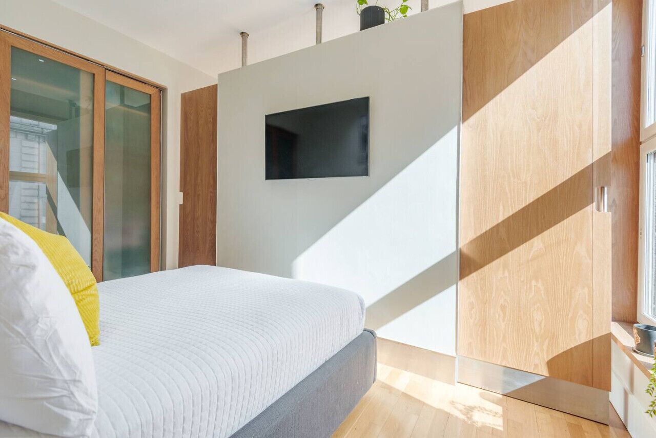 Une chambre à coucher moderne avec un lit, un téléviseur fixé au mur et un placard à portes coulissantes.