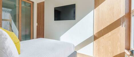 Une chambre à coucher moderne avec un lit, un téléviseur fixé au mur et un placard à portes coulissantes.