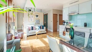 Un salon moderne avec un canapé, une table basse et une table à manger en verre. Il y a également un coin cuisine avec des placards et une cuisinière.