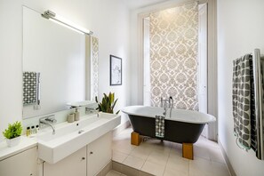 A modern bathroom with a freestanding bathtub, a large mirror, a sink with a vanity, and patterned wallpaper.