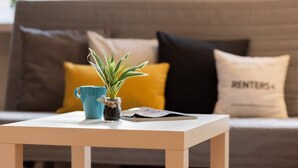 A small table with a potted plant and a blue mug in front of a sofa with yellow and black cushions.