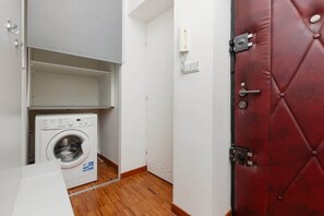 Un lavadero pequeño con lavadora, una puerta roja y una pared blanca.