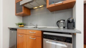 A compact kitchen with wooden cabinets, a dishwasher, a coffee maker, and a small potted plant.