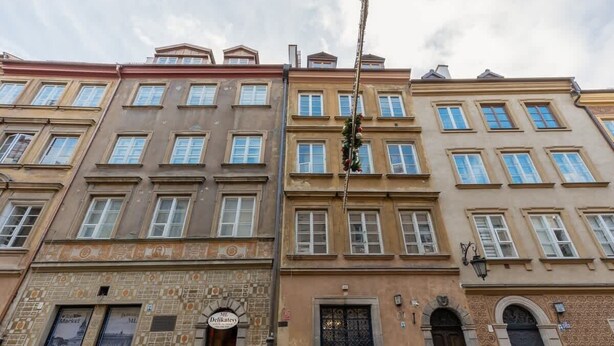 A row of historic buildings with uniform window patterns and a sign for 'Delicatessen' on the ground floor.