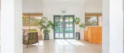 A spacious lobby with a reception desk, a seating area, and a large glass door leading outside.