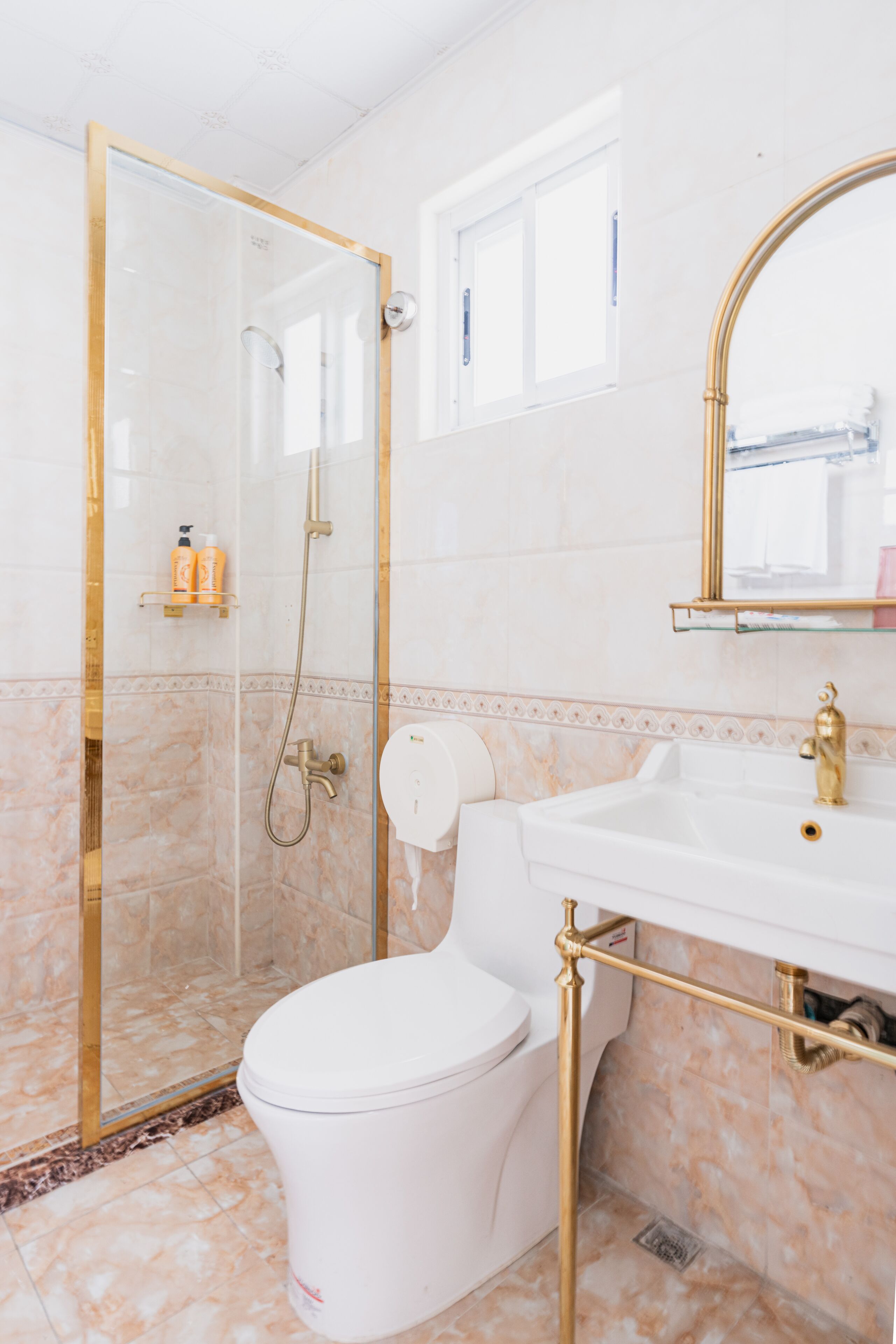 Une salle de bain dotée d’une douche à parois de verre, de toilettes blanches, d’un lavabo encadré d’or et d’un miroir également encadré d’or.
