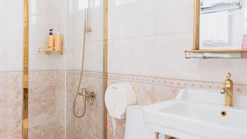 A bathroom with a glass-enclosed shower, a white toilet, a gold-framed sink, and a mirror with a gold frame.