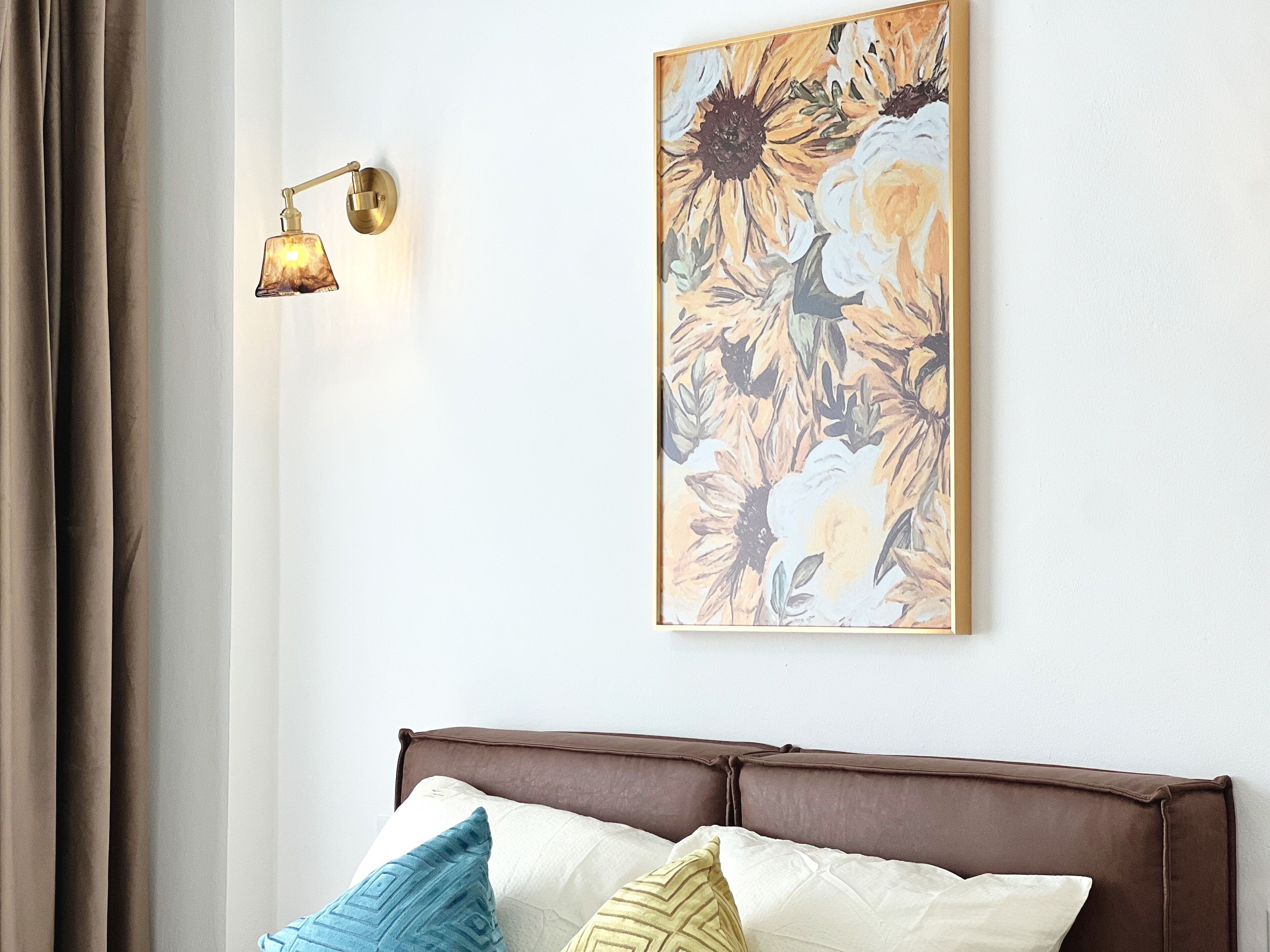 Ein Schlafzimmer mit braunem Kopfteil, einer Wandleuchte und einem Blumenbild.