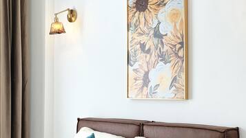 Et soveværelse med brun sengegavl, vægmonteret lampe og et blomsterbillede.