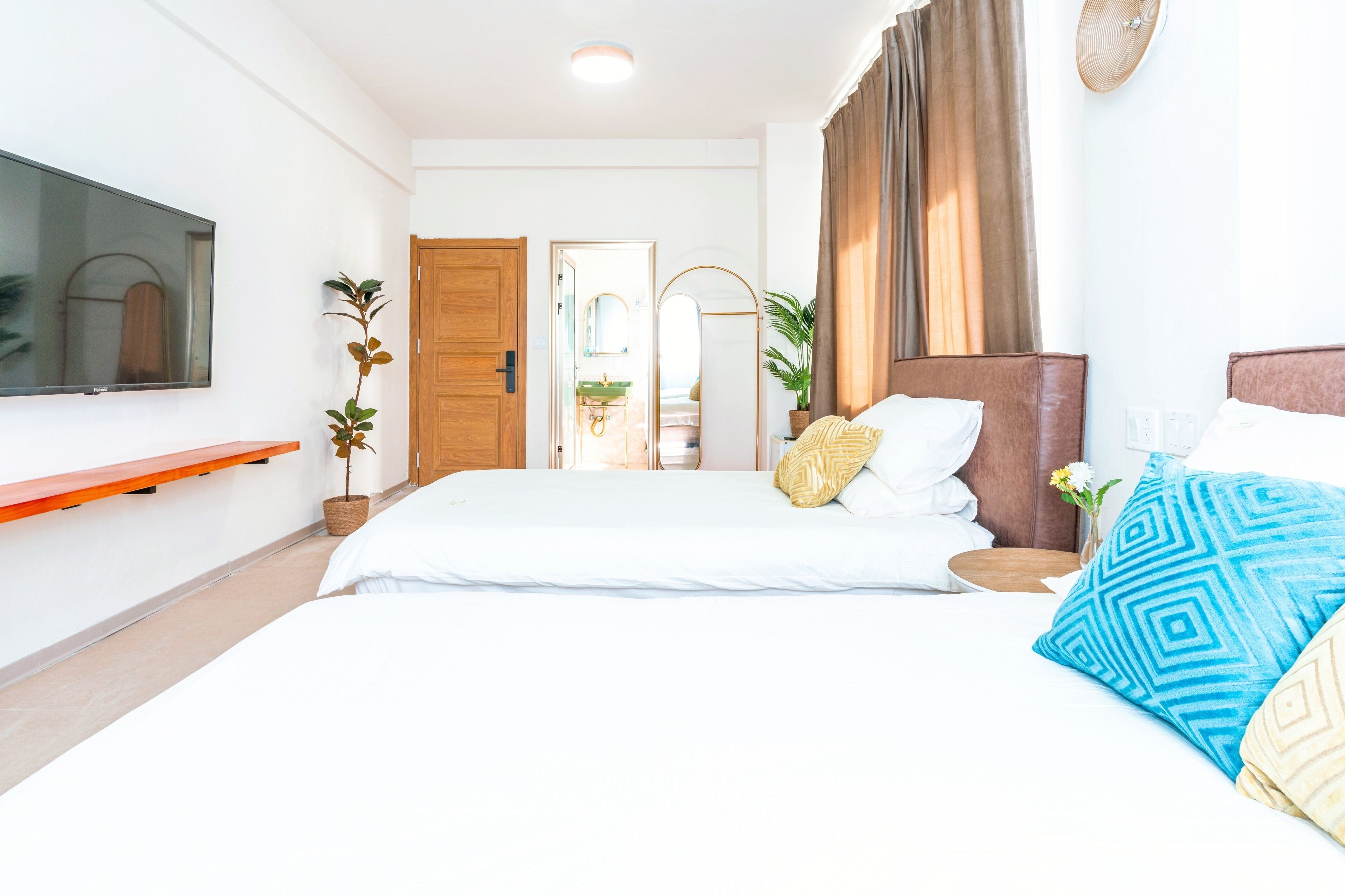 Habitación de hotel con una cama grande, un televisor montado en la pared, una puerta de madera y un baño visible a través de una puerta abierta.