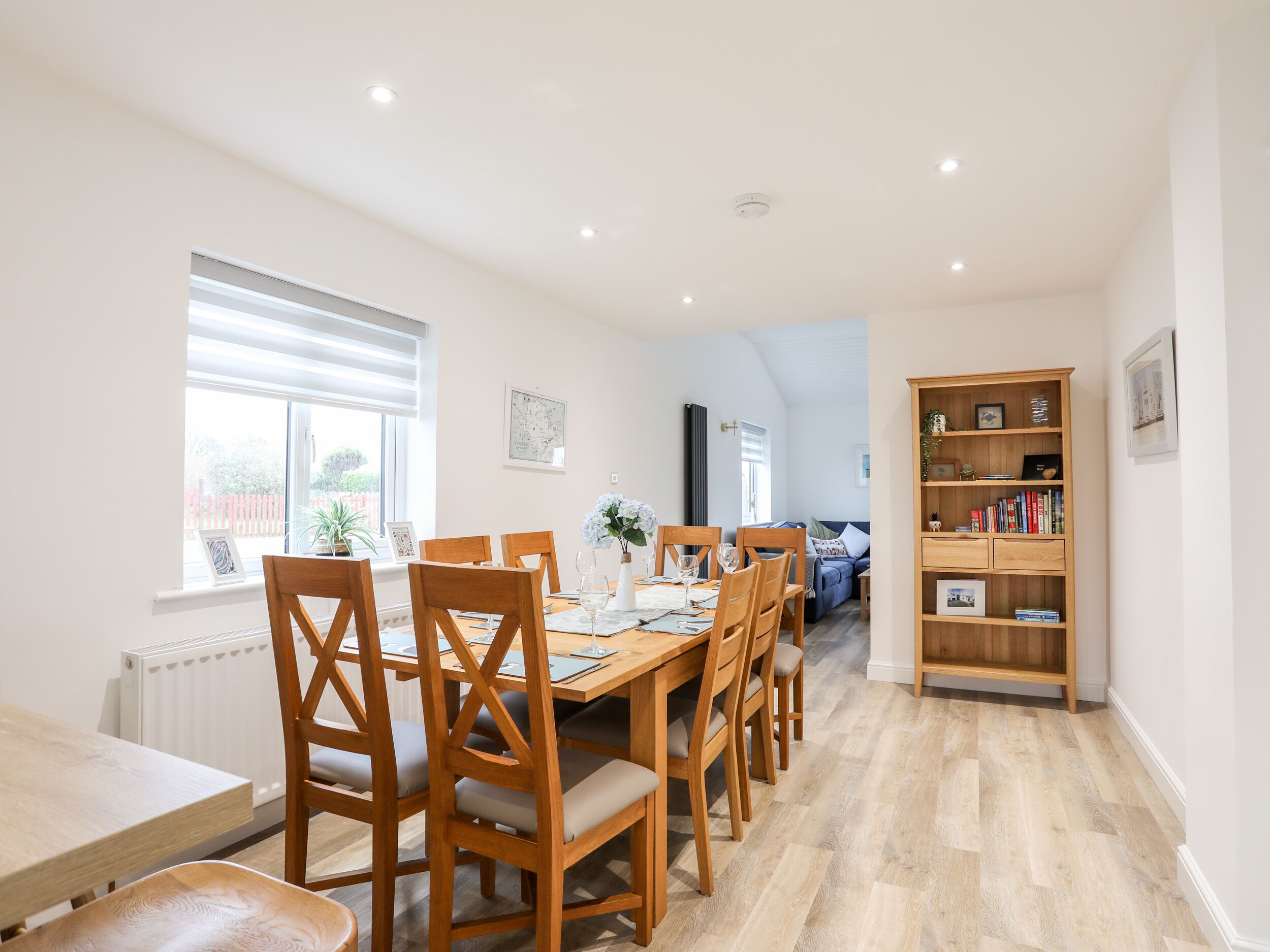 Un comedor con una mesa y sillas de madera, una estantería y vista al salón.