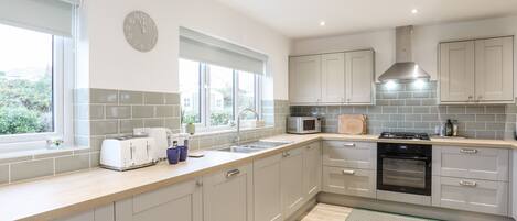 A modern kitchen with grey cabinets, a stainless steel sink, a microwave, and a stove. There are two windows providing natural light.