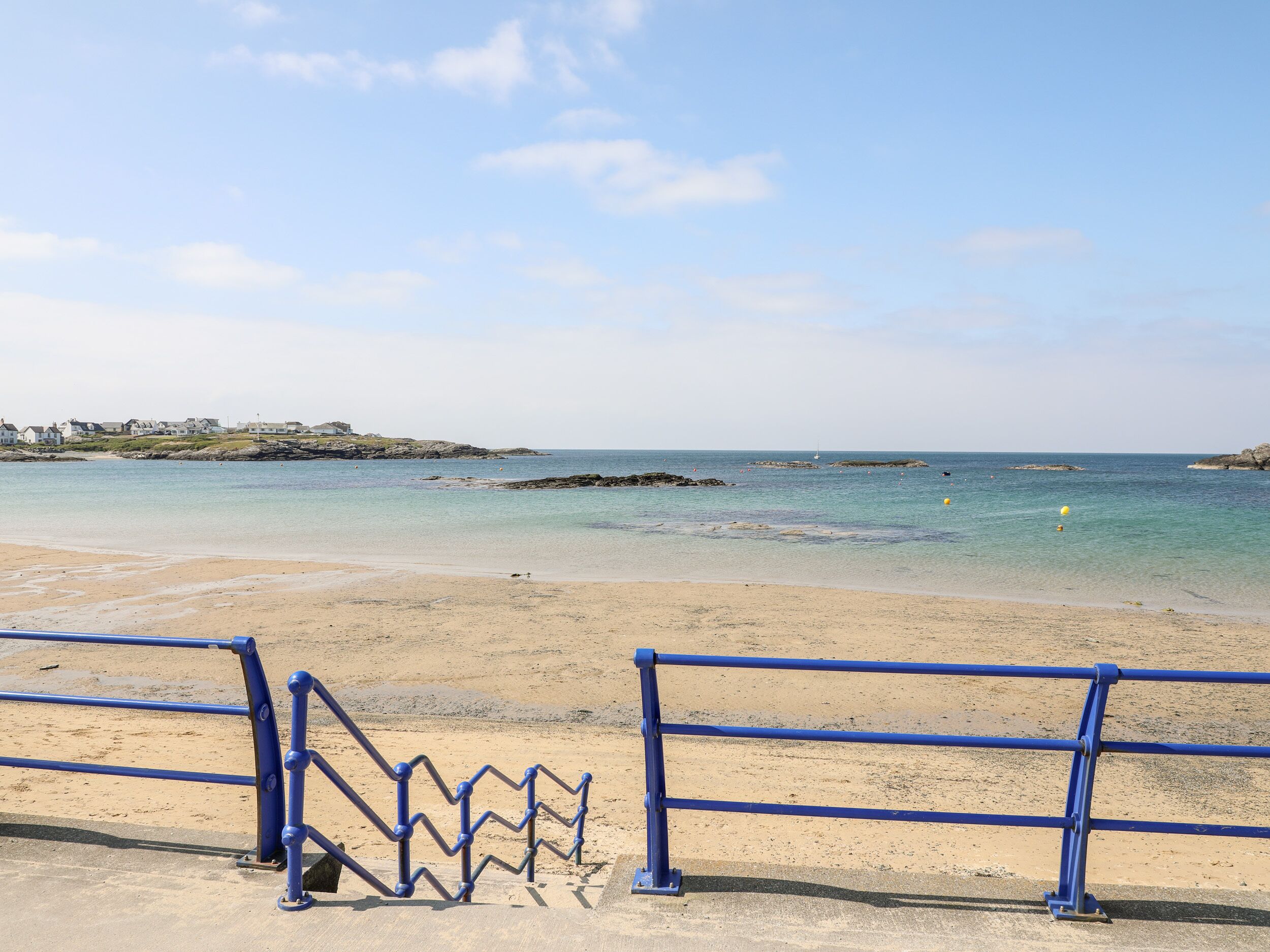 Una spiaggia con acqua cristallina, una riva sabbiosa e una ringhiera blu.