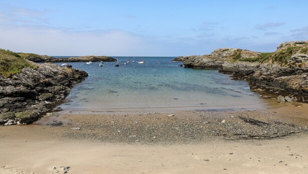 A rocky beach with clear water and boats. - Llwyn Eithin (Holyhead)